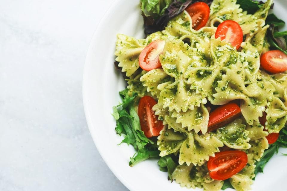 A white bowl of pasta with tomato and green basil.
